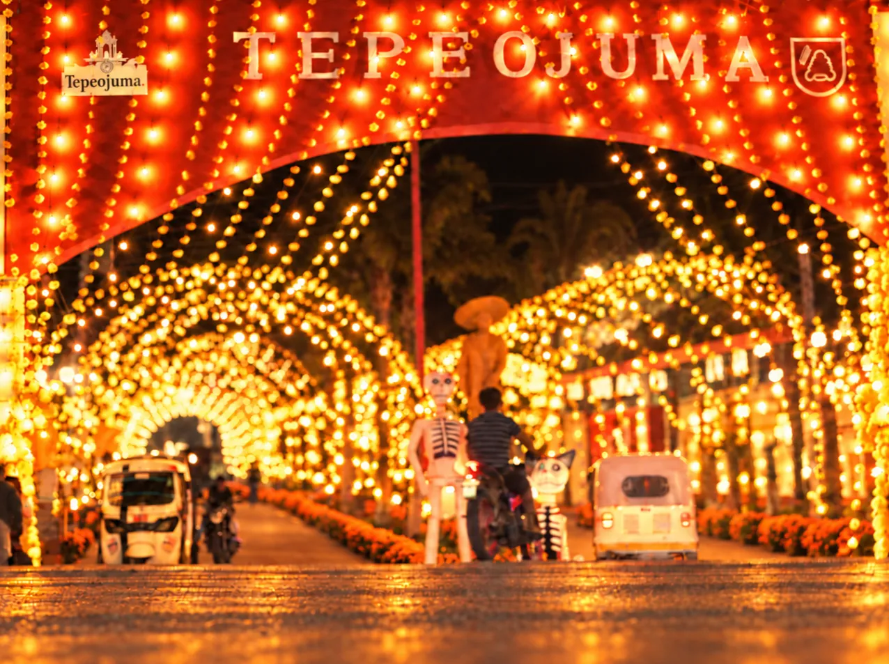 Arco iluminado con el nombre de Tepeojuma y túnel de luces sobre la avenida principal